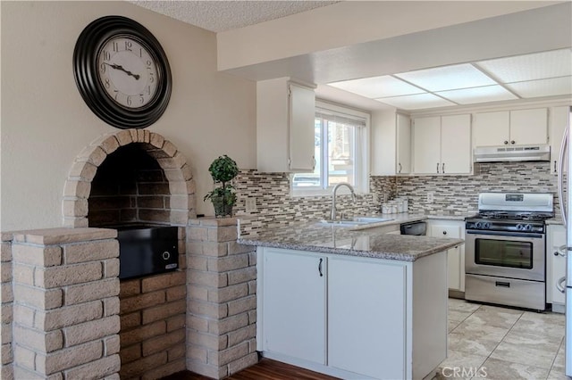 kitchen featuring stainless steel gas range, a sink, a peninsula, under cabinet range hood, and backsplash