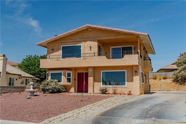 view of front of home with a balcony, stucco siding, and fence