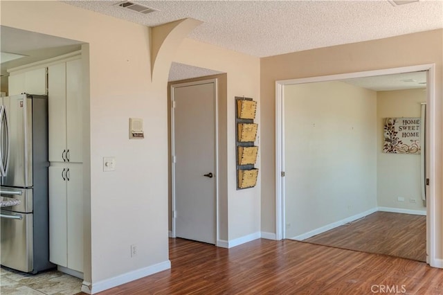 unfurnished room with light wood-style floors, a textured ceiling, baseboards, and arched walkways