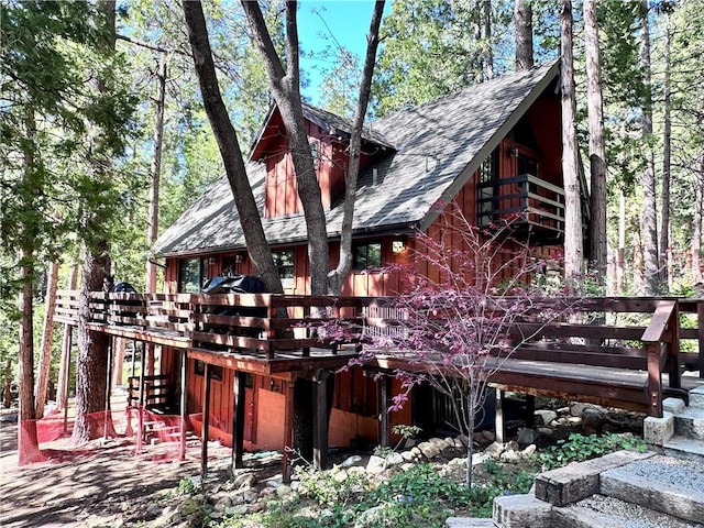 back of house with a deck, stairs, and roof with shingles