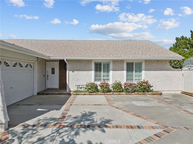 ranch-style home with stucco siding, an attached garage, a shingled roof, and a gate