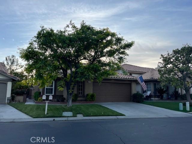 1321 Cypress Point Dr, Banning, CA 92220 - obstructed view of property with an attached garage, driveway, a tiled roof, a front yard, and stucco siding