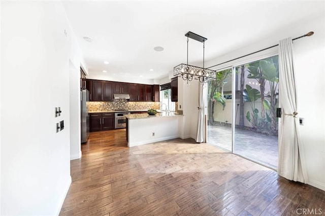 127 Lessay, Newport Coast, CA 92657 - kitchen featuring under cabinet range hood, appliances with stainless steel finishes, a chandelier, wood finished floors, and dark brown cabinets