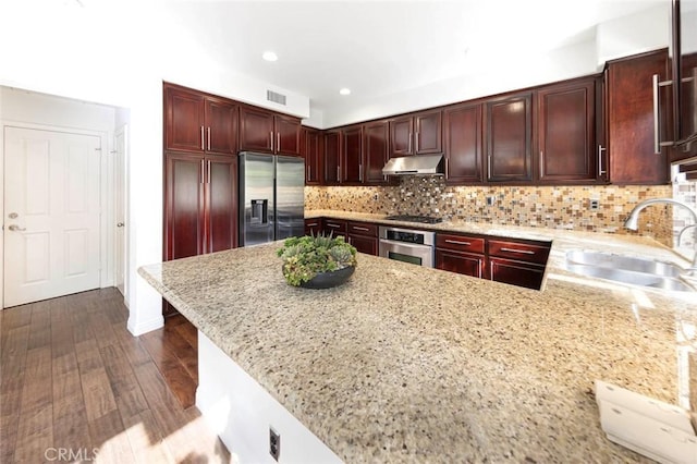 127 Lessay, Newport Coast, CA 92657 - kitchen with stainless steel appliances, under cabinet range hood, a sink, dark wood-style flooring, and light stone countertops