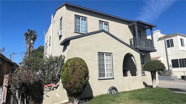 view of side of property with stucco siding, a balcony, and fence