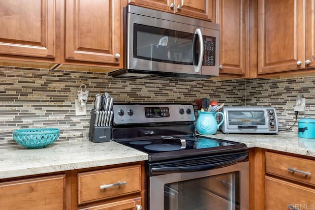 3552 Bartlett Ave, Oceanside, CA 92057 - kitchen featuring stainless steel appliances, backsplash, brown cabinetry, and light stone counters
