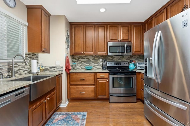 3552 Bartlett Ave, Oceanside, CA 92057 - kitchen featuring appliances with stainless steel finishes, brown cabinetry, light stone countertops, decorative backsplash, and light wood-type flooring