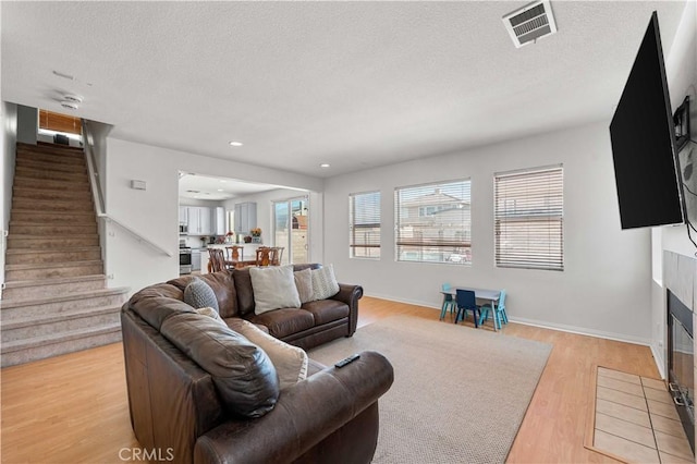 living room with stairway, light wood-style floors, healthy amount of natural light, a fireplace, and a textured ceiling