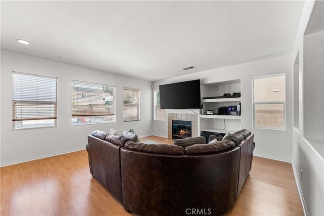living area with a tiled fireplace, light wood-style flooring, and baseboards