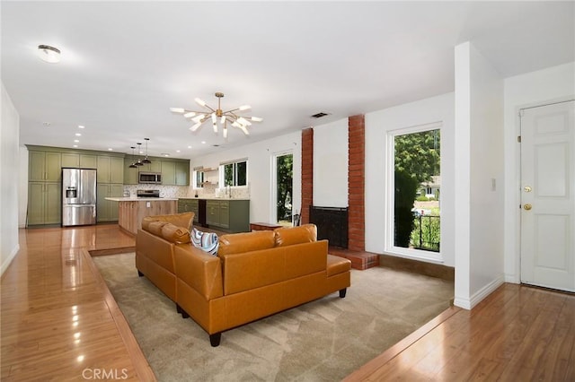 living room featuring a chandelier, light wood finished floors, baseboards, recessed lighting, and a brick fireplace