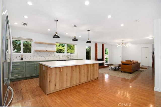 kitchen featuring freestanding refrigerator, green cabinets, a kitchen island, light wood-type flooring, and light countertops
