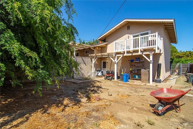 rear view of house featuring stucco siding, fence, and a wooden deck