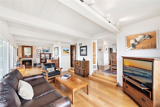 living room with a large fireplace, light wood-style flooring, and beam ceiling