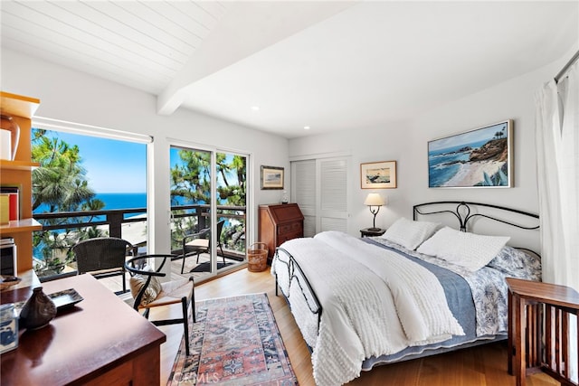 bedroom with light wood-style floors, a water view, recessed lighting, a closet, and beamed ceiling