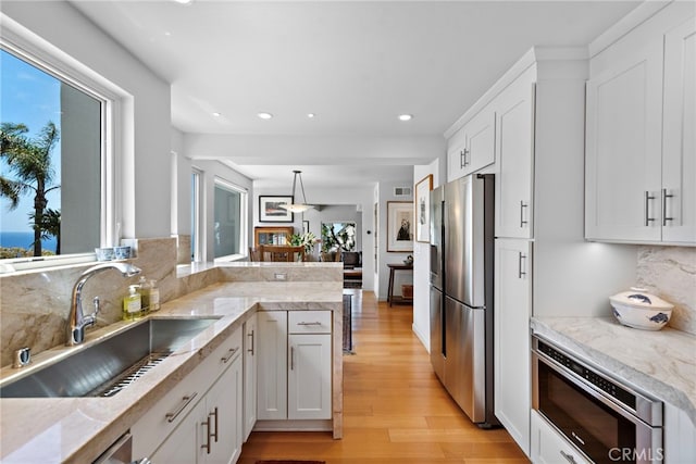 kitchen featuring stainless steel fridge with ice dispenser, a sink, built in microwave, light wood-style floors, and recessed lighting