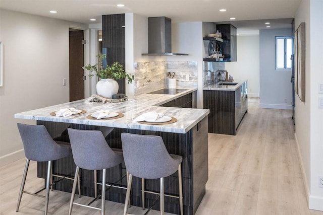 kitchen with wall chimney exhaust hood, modern cabinets, a sink, a kitchen bar, and tasteful backsplash