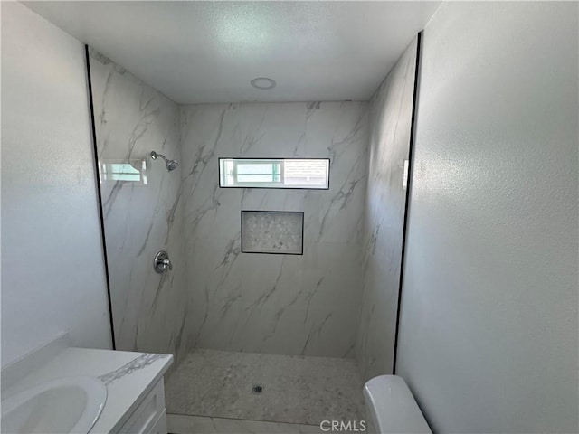 bathroom featuring toilet, a marble finish shower, and vanity