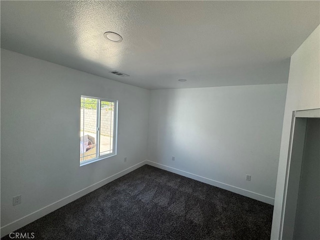 empty room with dark carpet, baseboards, and a textured ceiling