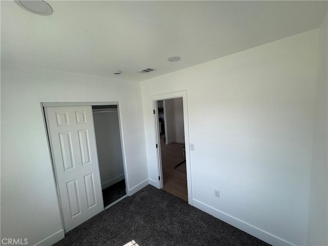 unfurnished bedroom with baseboards, dark carpet, and a closet