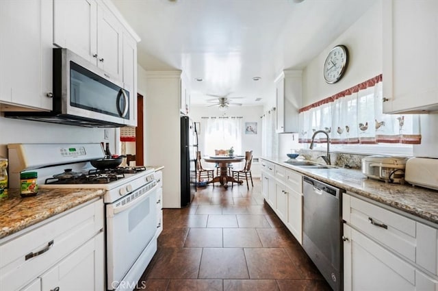 kitchen featuring appliances with stainless steel finishes, a sink, a ceiling fan, white cabinetry, and dark tile patterned floors