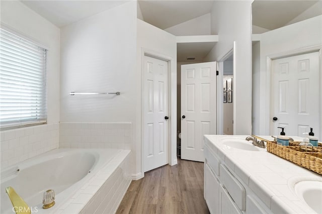 full bath with wood finished floors, a garden tub, double vanity, and vaulted ceiling