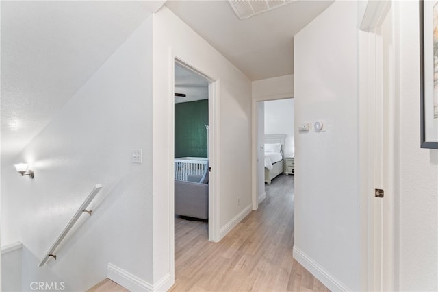 corridor with an upstairs landing, light wood-type flooring, and baseboards