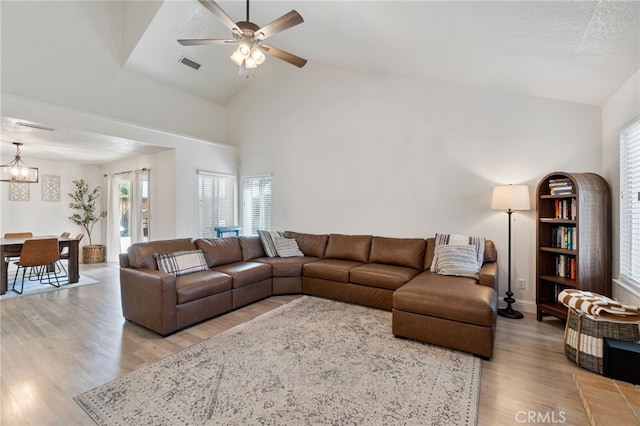 living room with light wood finished floors, a ceiling fan, high vaulted ceiling, a chandelier, and baseboards