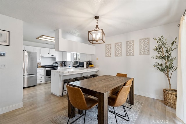 dining room with light wood-style flooring, a chandelier, and baseboards