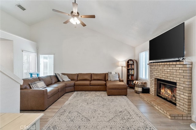 living area featuring a ceiling fan, a fireplace, light wood-style floors, and high vaulted ceiling