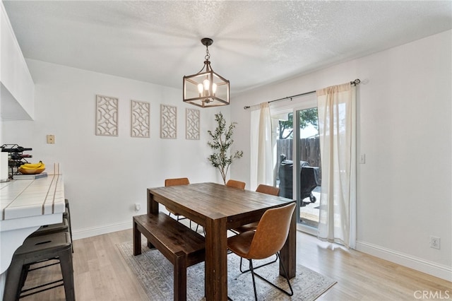 dining area featuring light wood finished floors, a chandelier, baseboards, and a textured ceiling