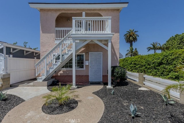 doorway to property with stucco siding, fence, and brick siding