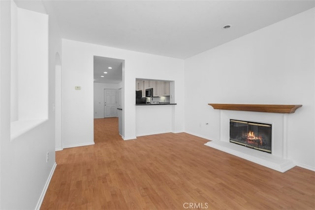 14726 Burgundy Pl, Chino Hills, CA 91709 - unfurnished living room with light wood-style floors, a glass covered fireplace, arched walkways, baseboards, and recessed lighting