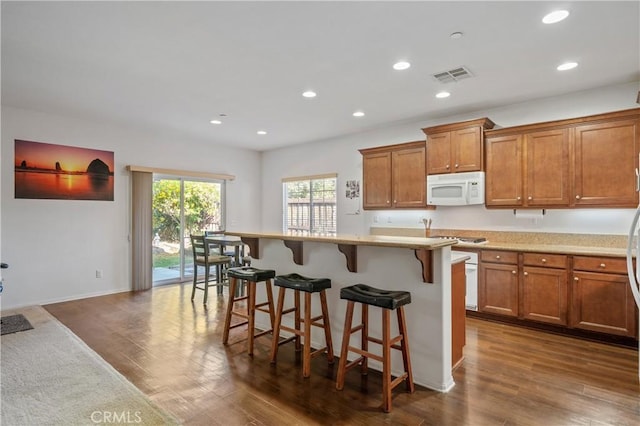 40991 Bankhall St, Lake Elsinore, CA 92532 - kitchen with white microwave, brown cabinetry, dark wood-style floors, recessed lighting, and a breakfast bar area