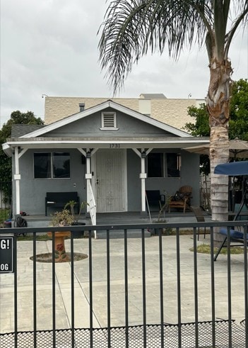 view of front of house with stucco siding, fence, and covered porch