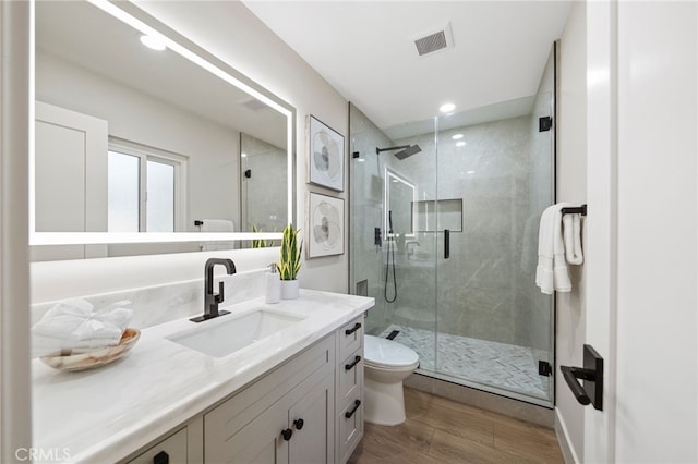 bathroom featuring wood finished floors, a stall shower, toilet, vanity, and recessed lighting