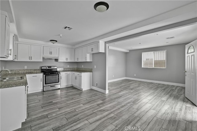 202 E 116th St, Los Angeles, CA 90061 - kitchen with stainless steel gas stove, a sink, under cabinet range hood, dark stone countertops, and open floor plan