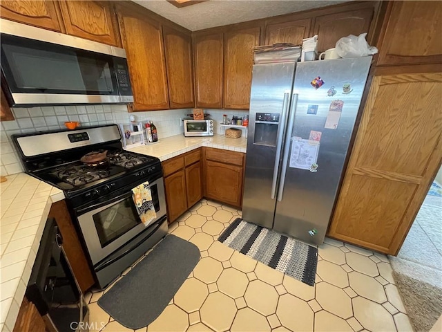 4041 Bluff Pl Unit 2, San Pedro, CA 90731 - kitchen featuring stainless steel appliances, tile countertops, backsplash, brown cabinets, and light flooring