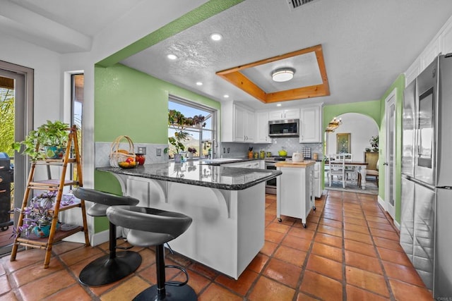 979 Canyon Heights Rd, Fallbrook, CA 92028 - kitchen featuring stainless steel appliances, a tray ceiling, backsplash, a peninsula, and white cabinets
