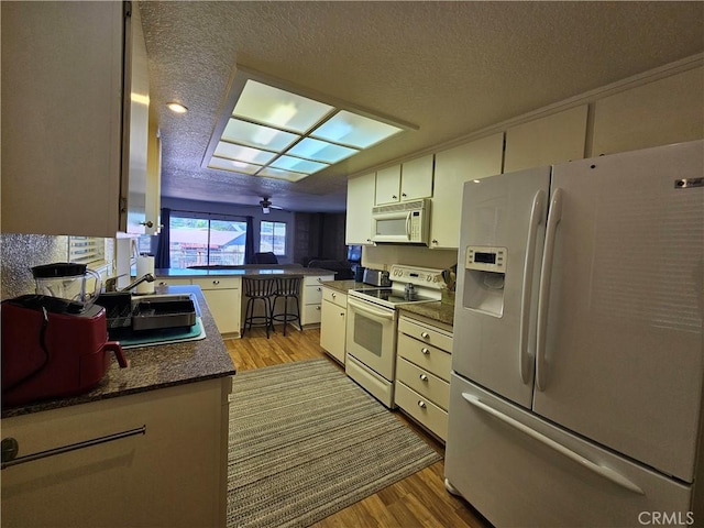 kitchen with white appliances, wood finished floors, a textured ceiling, dark countertops, and white cabinets
