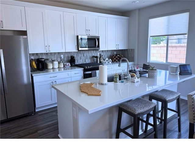 31832 Gimbal Way, Winchester, CA 92596 - kitchen with stainless steel appliances, dark wood-type flooring, white cabinets, decorative backsplash, and a kitchen bar