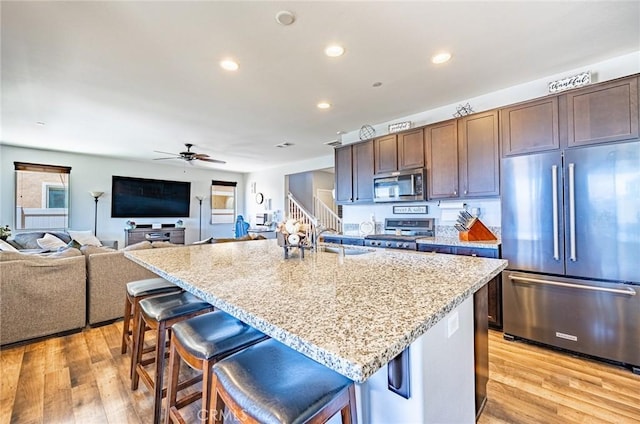1357 Bannock St, Beaumont, CA 92223 - kitchen featuring appliances with stainless steel finishes, light stone counters, ceiling fan, light wood-style floors, and a breakfast bar area