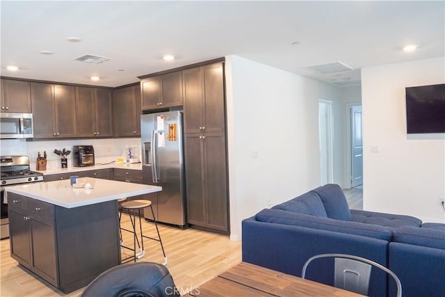 15148 Ridge Ln Unit 4, Fontana, CA 92336 - kitchen featuring appliances with stainless steel finishes, light wood finished floors, open floor plan, a kitchen bar, and dark brown cabinets