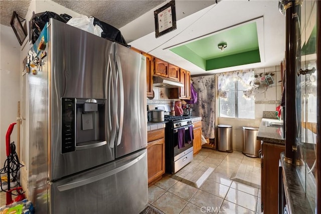1165 E 24th St, Los Angeles, CA 90011 - kitchen with stainless steel appliances, under cabinet range hood, brown cabinetry, light tile patterned flooring, and decorative backsplash