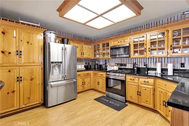 kitchen with stainless steel appliances, light wood finished floors, dark countertops, and glass insert cabinets