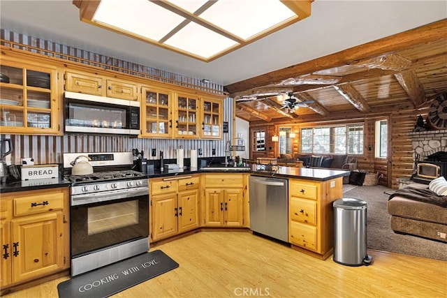 kitchen featuring stainless steel appliances, open floor plan, a peninsula, light wood finished floors, and beamed ceiling