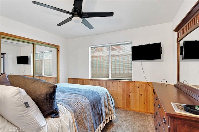 carpeted bedroom featuring wood walls, a wainscoted wall, and ceiling fan