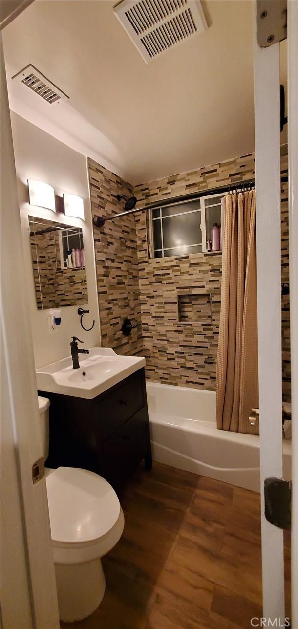 bathroom with shower / bath combination with curtain, wood finished floors, vanity, and toilet