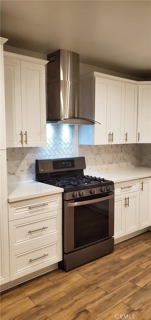 kitchen with stainless steel range with gas cooktop, wall chimney exhaust hood, light countertops, white cabinets, and light wood-style flooring