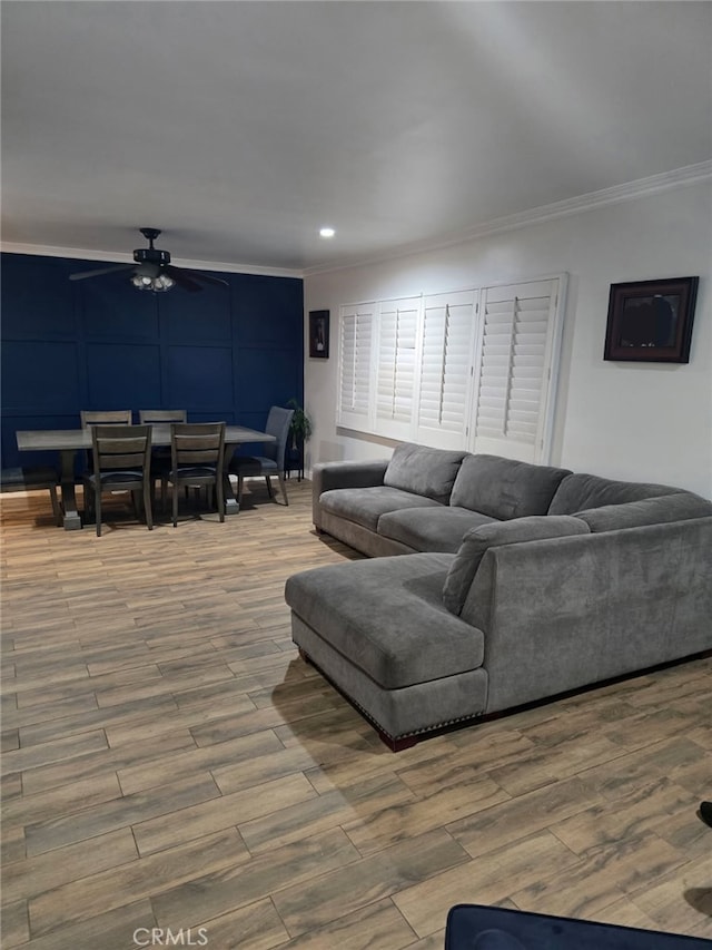 living area with crown molding, ceiling fan, wood finished floors, recessed lighting, and a decorative wall
