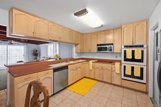 kitchen with light brown cabinetry, stainless steel appliances, light tile patterned floors, a peninsula, and a sink